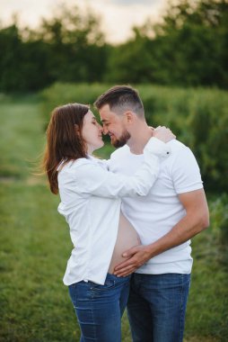 Mutlu ve genç hamile çift doğada sarılıyorlar..