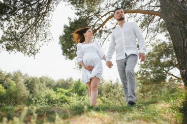 Mutlu ve genç hamile çift doğada sarılıyorlar..