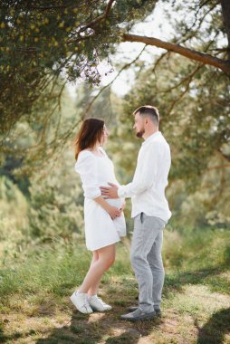 Mutlu ve genç hamile çift doğada sarılıyorlar..