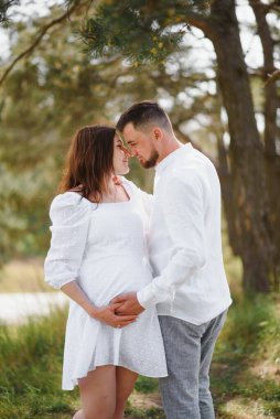 Mutlu ve genç hamile çift doğada sarılıyorlar..