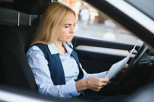 Fashion business woman with financial papers by her car.