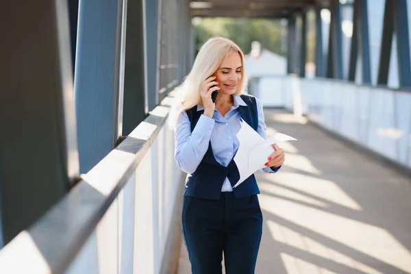 Business Woman With Phone Near Office. Portrait Of Beautiful Smiling Female In Fashion Office Clothes Talking On Phone While Standing Outdoors. Phone Communication. High Quality Image