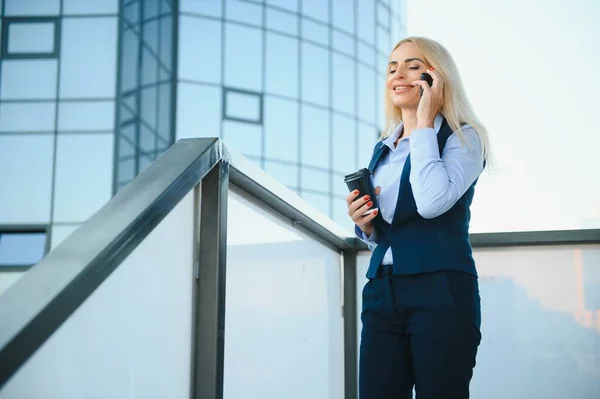 Business Woman With Phone Near Office. Portrait Of Beautiful Smiling Female In Fashion Office Clothes Talking On Phone While Standing Outdoors. Phone Communication. High Quality Image