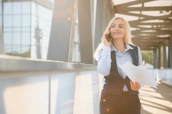 Business Woman With Phone Near Office. Portrait Of Beautiful Smiling Female In Fashion Office Clothes Talking On Phone While Standing Outdoors. Phone Communication. High Quality Image