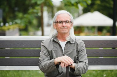 Yaşlı bir adam bir bahar parkında bastonla yürüyor.