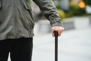 Yaşlı bir adam bir bahar parkında bastonla yürüyor.