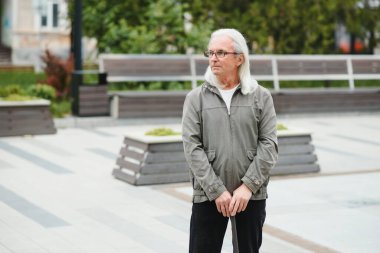 Yaşlı bir adam bir bahar parkında bastonla yürüyor.