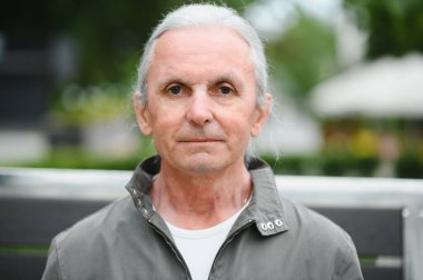 Yaşlı gri saçlı adam yaz parkındaki bankta dinleniyor..