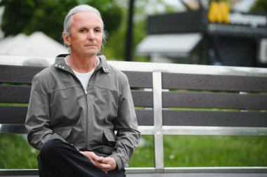 Yaşlı, kır saçlı adam şehirde dikiliyor.