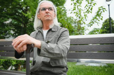Yaşlı gri saçlı adam yaz parkındaki bankta dinleniyor..