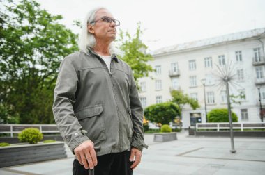 Park yerinde dinlenirken elinde baston tutan yaşlı adamın portresi.