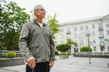Park yerinde dinlenirken elinde baston tutan yaşlı adamın portresi.