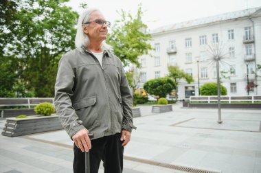 Yaşlı bir adam bir bahar parkında bastonla yürüyor.