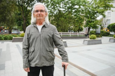 Park yerinde dinlenirken elinde baston tutan yaşlı adamın portresi.