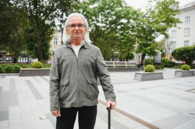 Yaşlı bir adam bir bahar parkında bastonla yürüyor.
