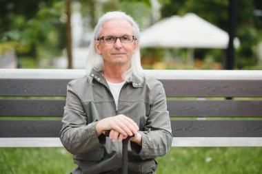 Yaşlı gri saçlı adam yaz parkındaki bankta dinleniyor..