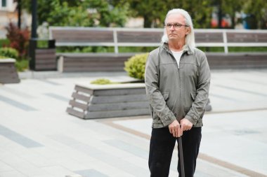 Park yerinde dinlenirken elinde baston tutan yaşlı adamın portresi.