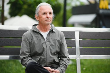 Yaşlı gri saçlı adam yaz parkındaki bankta dinleniyor..