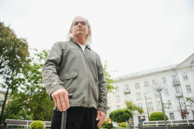 Park yerinde dinlenirken elinde baston tutan yaşlı adamın portresi.