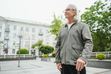 Yaşlı bir adam bir bahar parkında bastonla yürüyor.