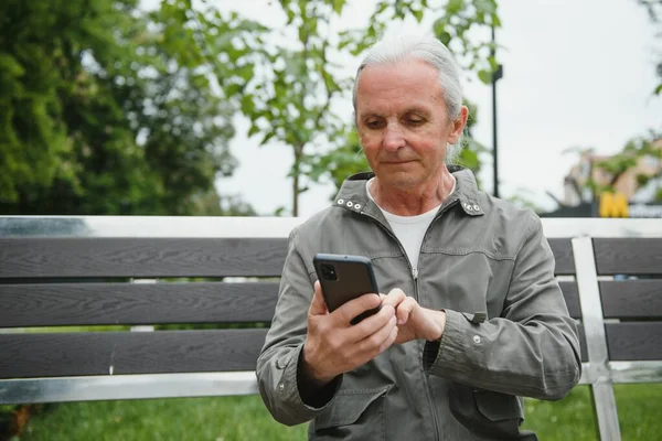 Old man browsing app on smartphone, outdoor in park.