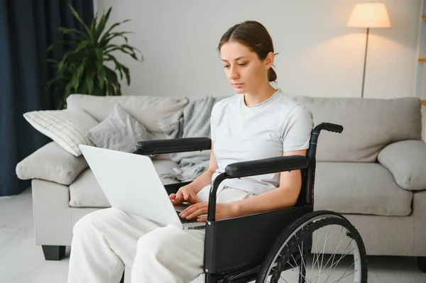 woman in a wheelchair works on the laptop PC in the home office with an assistance dog as a companion.