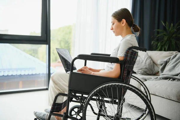 Female freelance programmer sitting in wheelchair and using computers while coding web game at home