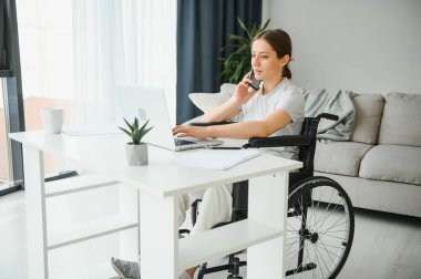 Evde internet oyunu yazarken tekerlekli sandalyede oturan ve bilgisayar kullanan serbest çalışan bir kadın programcı.
