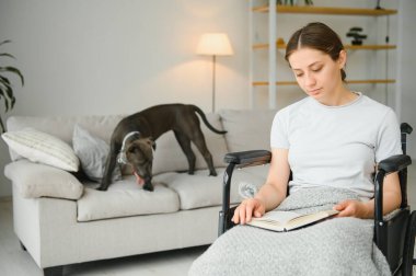 Tekerlekli sandalyedeki kadın evde kitap okuyor..