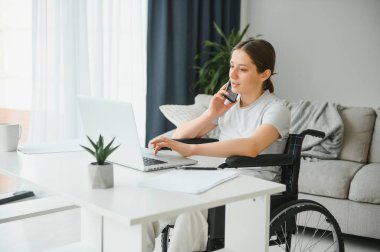 Evde internet oyunu yazarken tekerlekli sandalyede oturan ve bilgisayar kullanan serbest çalışan bir kadın programcı.
