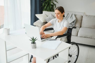 Evde internet oyunu yazarken tekerlekli sandalyede oturan ve bilgisayar kullanan serbest çalışan bir kadın programcı.