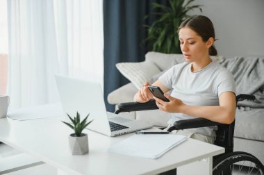 Evde internet oyunu yazarken tekerlekli sandalyede oturan ve bilgisayar kullanan serbest çalışan bir kadın programcı.
