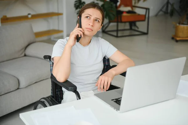 woman in a wheelchair works on the laptop PC in the home office with an assistance dog as a companion.