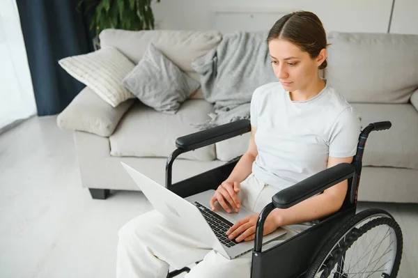Female freelance programmer sitting in wheelchair and using computers while coding web game at home