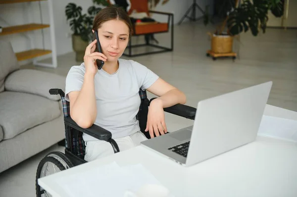 woman in a wheelchair works on the laptop PC in the home office with an assistance dog as a companion.