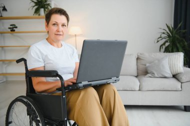 Orta yaşlı, gri saçlı, engelli bir kadın tekerlekli sandalyede otururken görüntülü konuşma yapıyor.