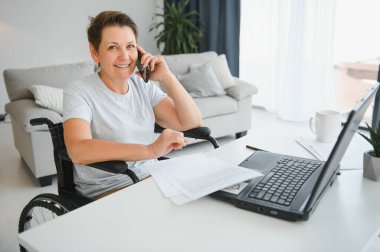 Evde tekerlekli sandalyede oturan orta yaşlı kadın dizüstü bilgisayar kullanıyor..
