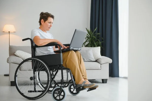 中年妇女坐在轮椅上使用笔记本电脑 — 图库照片