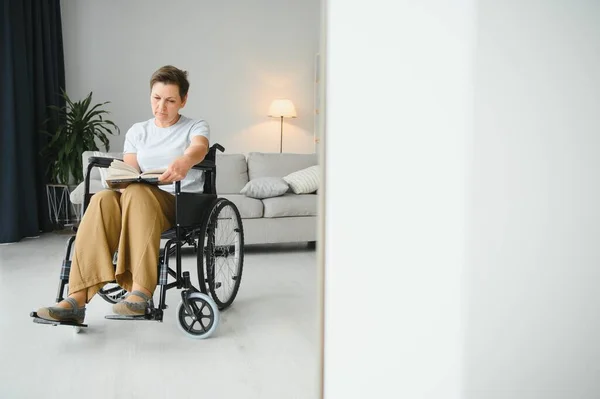 Strzał Starszej Kobiety Siedzącej Wózku Inwalidzkim Czytającej Książkę Domu — Zdjęcie stockowe