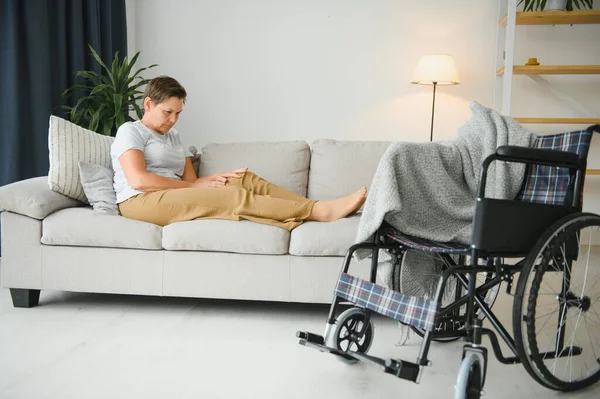 Brunette woman on couch near wheelchair.