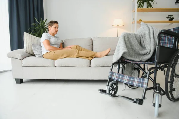 Brunette woman on couch near wheelchair.