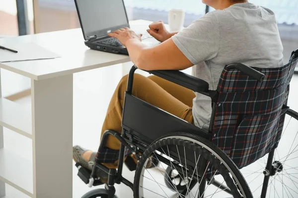 Positive elderly woman in wheelchair working on laptop, IT freelancer, online.