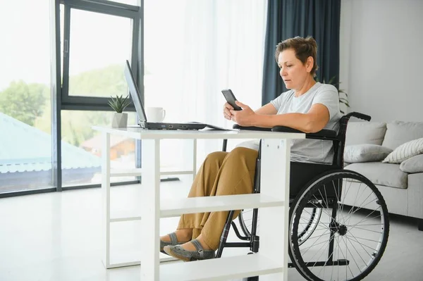 Positive elderly woman in wheelchair working on laptop, IT freelancer, online.