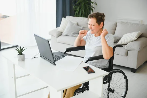 Kobieta Średnim Wieku Pomocą Laptopa Siedzi Wózku Inwalidzkim Domu — Zdjęcie stockowe