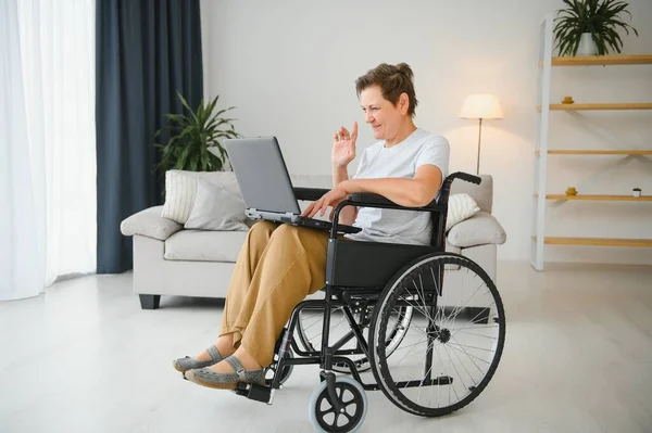 Orta yaşlı, gri saçlı, engelli bir kadın tekerlekli sandalyede otururken görüntülü konuşma yapıyor.