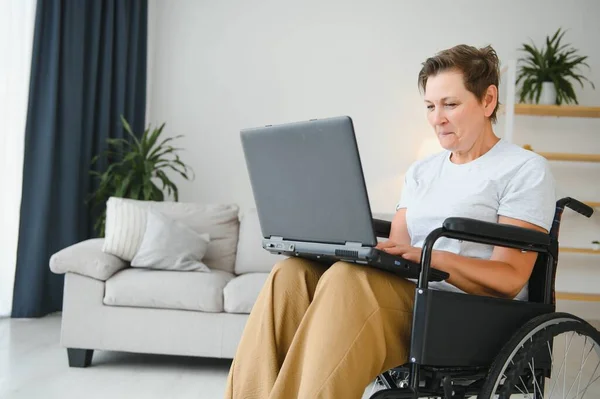 积极的老年妇女在轮椅上工作的笔记本电脑 它的自由职业者 — 图库照片