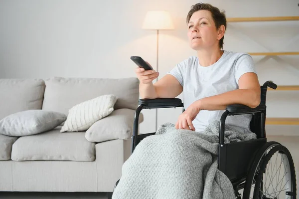 坐轮椅的妇女使用电视遥控器 — 图库照片