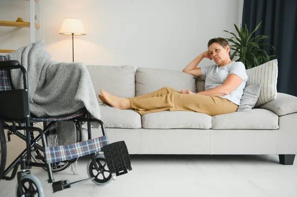 Brunette woman on couch near wheelchair.