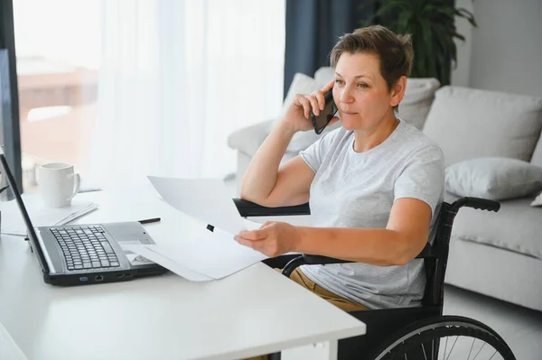 Positive elderly woman in wheelchair working on laptop, IT freelancer, online.
