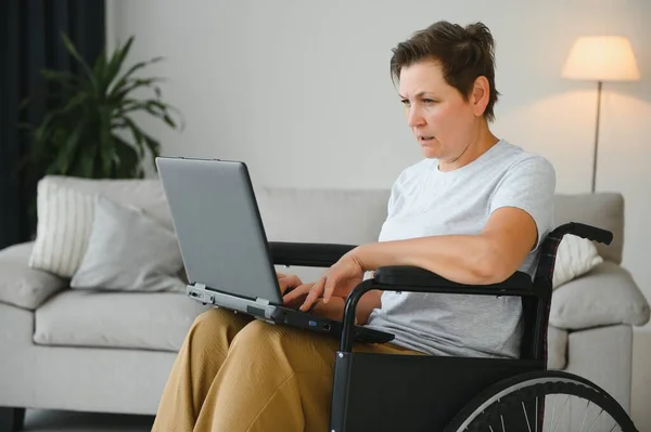 中年妇女坐在轮椅上使用笔记本电脑 — 图库照片